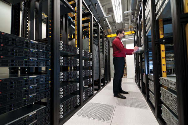 Young IT administrator installing a new rack mount server. Large scale storage server is also seen.